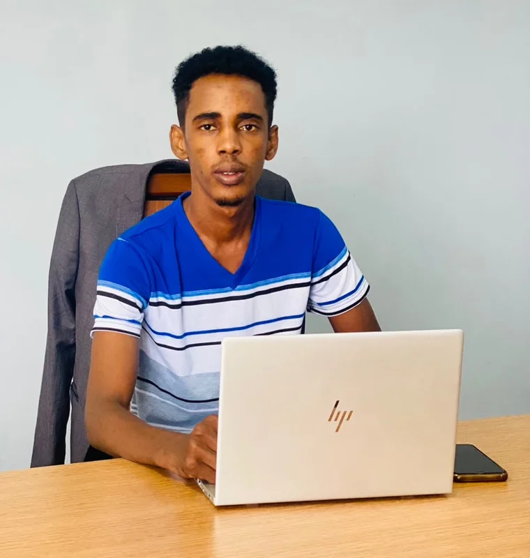 Abakar Idriss Kokoï à son poste de travail, devant un ordinateur portable ouvert.